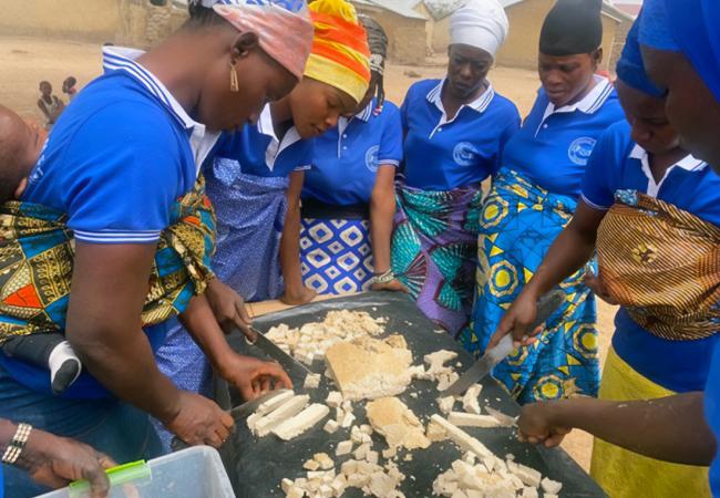 Village Savings and Loans Association /Mother to Mother Support Groups(VSLA/MTMSGs) in a cooking demonstration of the preparation of soya meal outdoors.