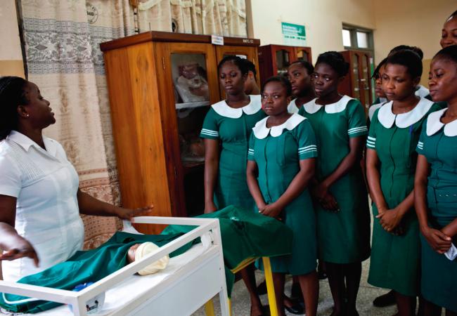 Group of health workers watching a trainer show them how to work with a newborn in a classroom.